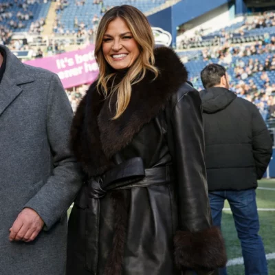 Woman wearing a black leather coat with fur collar and belt, standing in a stadium with a stylish winter outfit